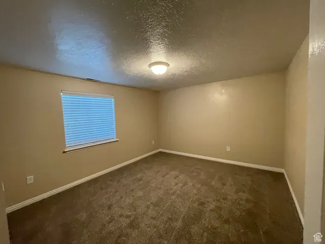 Unfurnished room featuring a textured ceiling and dark carpet