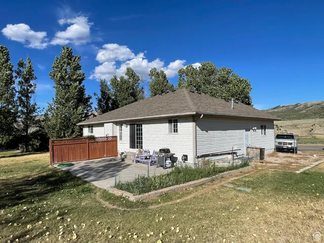 Rear view of property featuring a patio, a shingled roof, and a lawn
