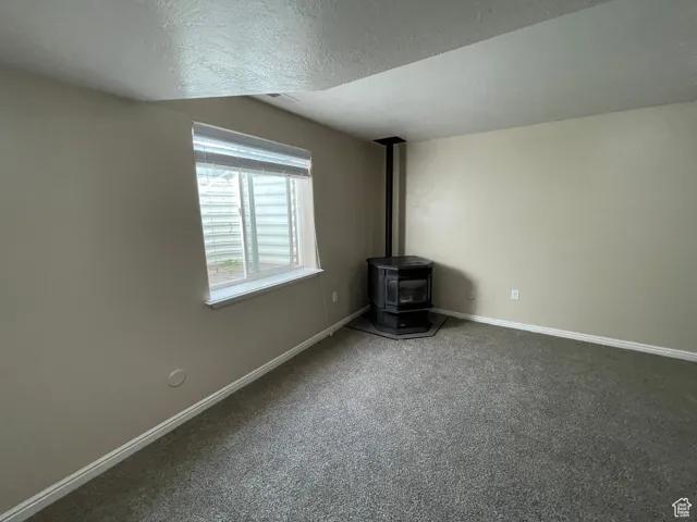 Unfurnished living room featuring a wood stove, carpet, and a textured ceiling