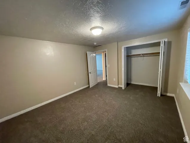 Unfurnished bedroom with dark carpet, a textured ceiling, and a closet