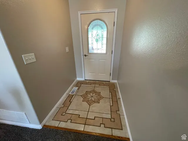 Doorway with light tile patterned floors and a textured wall