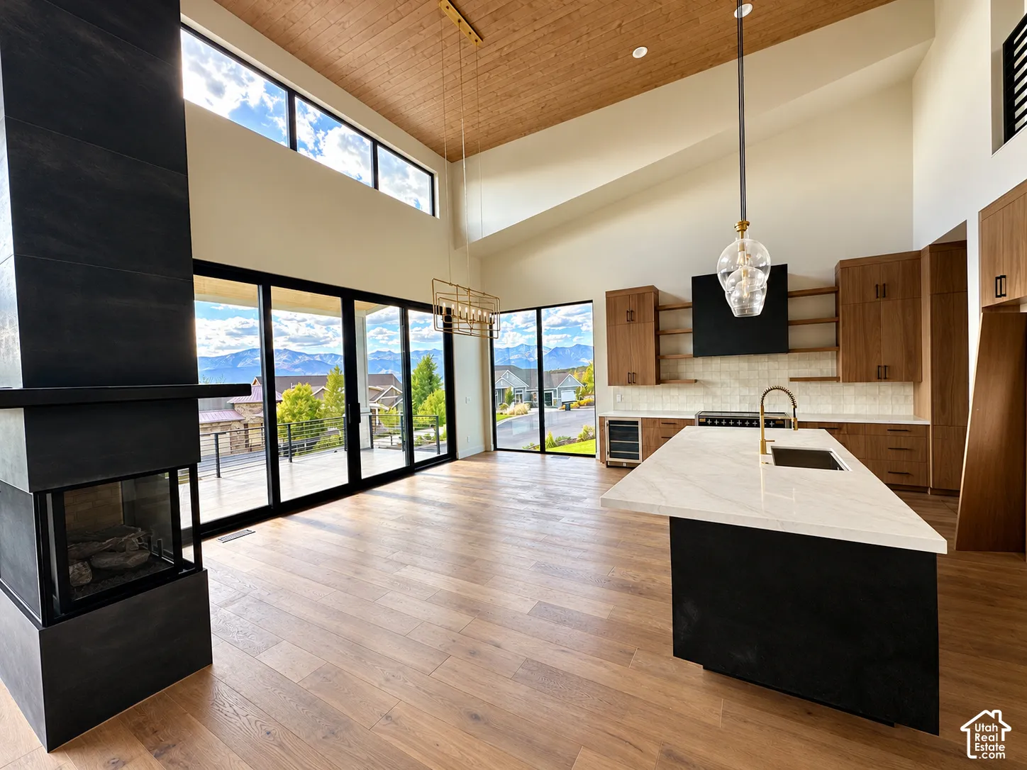 Modern open-concept kitchen and living area featuring warm wood-finish flooring, vaulted wood ceiling with skylights, and expansive black-framed glass doors opening to scenic mountain vistas