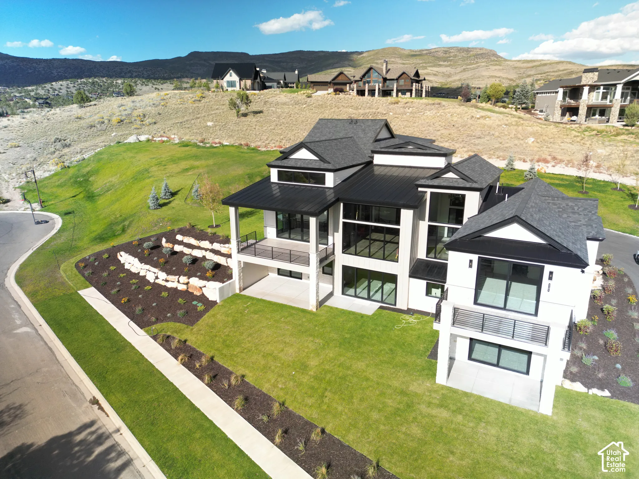 Contemporary architectural design featuring expansive windows, multiple balconies with metal railings, a dark shingle roof, and a meticulously landscaped yard with terraced rock walls