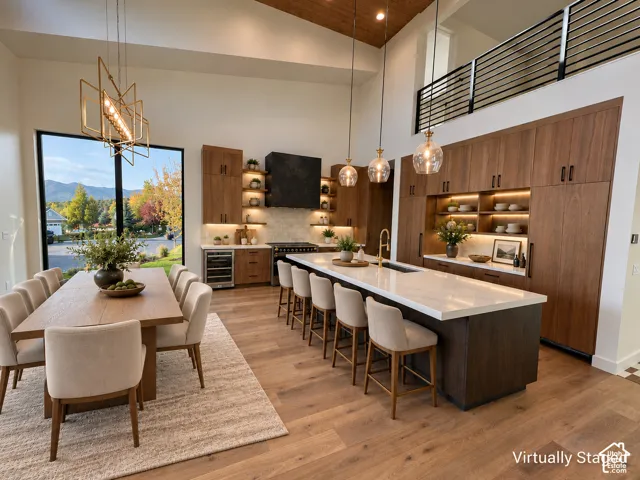Gourmet kitchen with wood-finish flooring, two-story vaulted ceiling, custom wood cabinetry, a large kitchen island with seating, and a built-in wine cooler