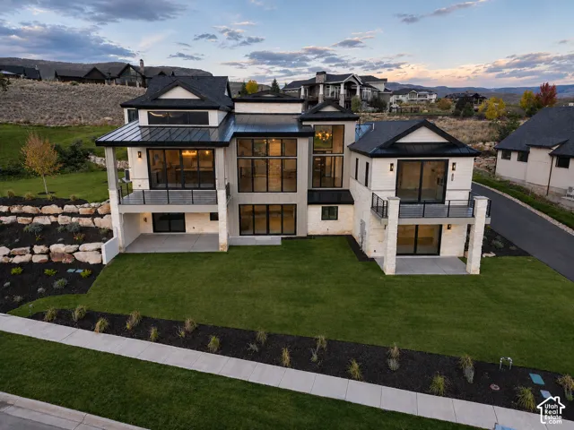 Contemporary exterior with multiple balconies featuring glass railings, a stone retaining wall, extensive landscaping, and a manicured lawn