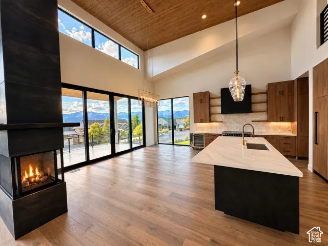 Vaulted wood-finish ceiling, expansive glass sliding doors, integrated fireplace with a multi-sided glass enclosure, wood-finish flooring, and a kitchen island with a single basin sink