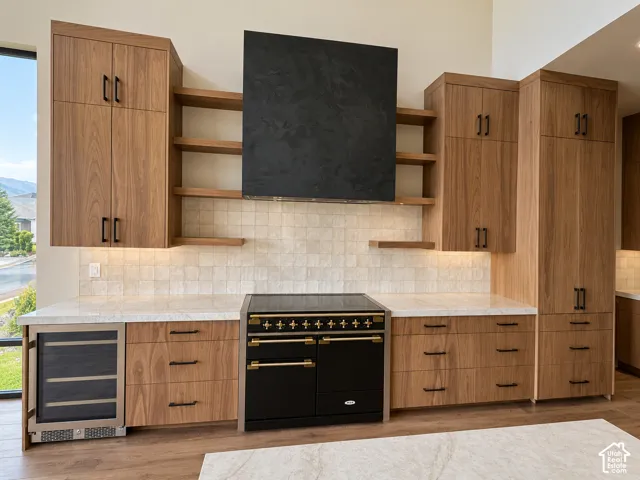 Wood-finish cabinetry, light-toned countertops, tile backsplash, built-in wine refrigerator, and a freestanding range with a black hood