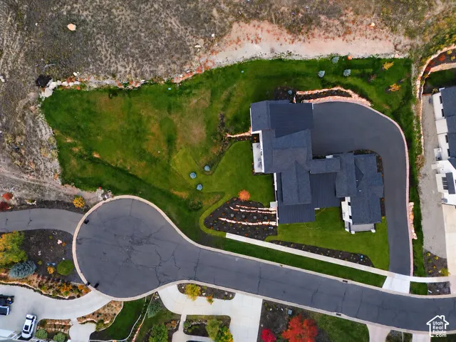 Modern residence with a dark roof and light-colored siding, extensive paved driveway, manicured lawn, and natural landscaping borders