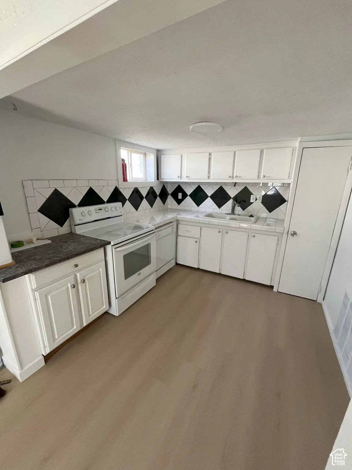 Kitchen featuring white cabinets, white appliances, backsplash, light wood finished floors, and dark stone counters