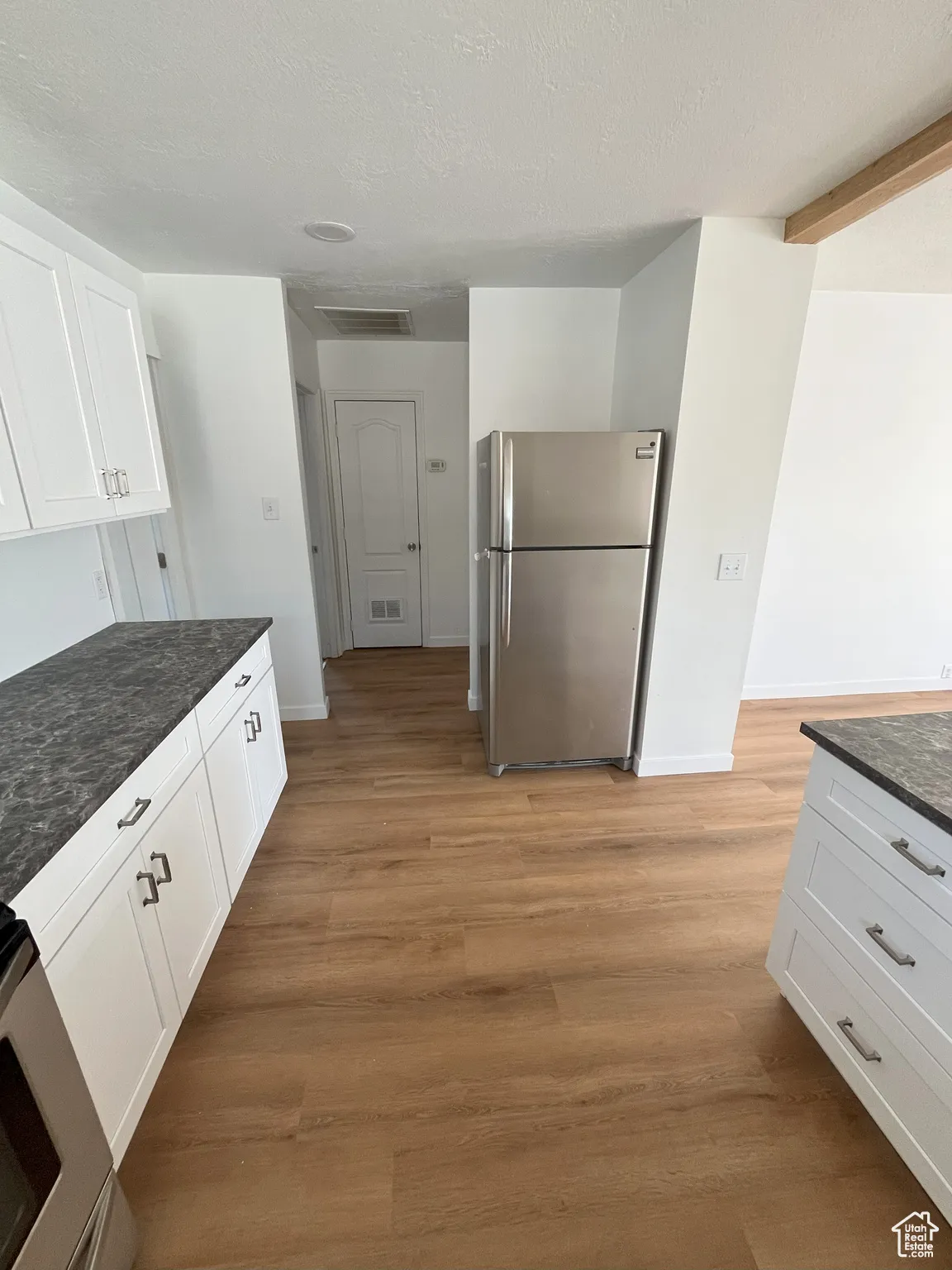 Kitchen with white cabinetry, appliances with stainless steel finishes, light wood-style flooring, dark stone counters, and a textured ceiling