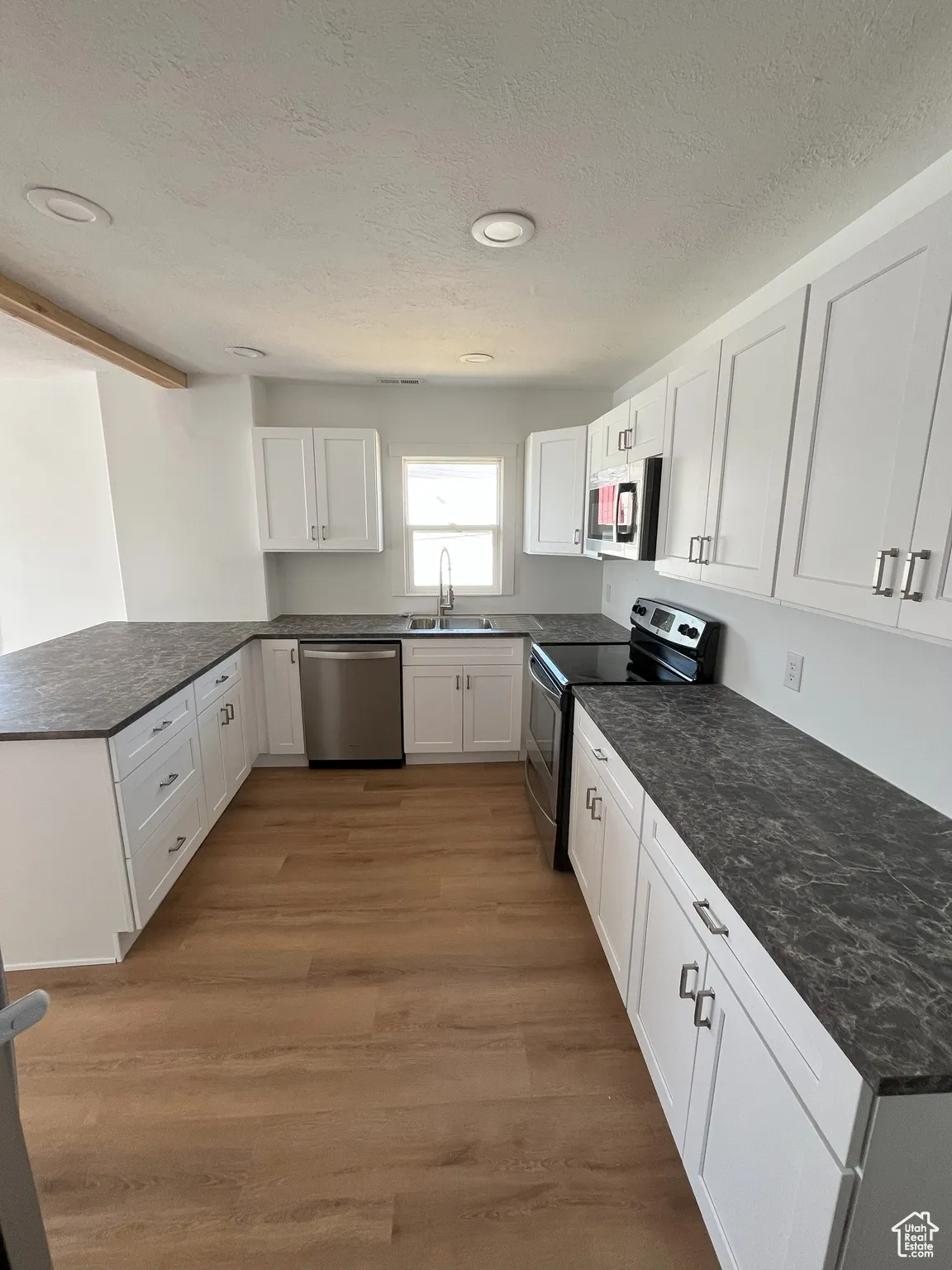 Kitchen featuring appliances with stainless steel finishes, white cabinetry, a peninsula, a textured ceiling, and light wood-style floors
