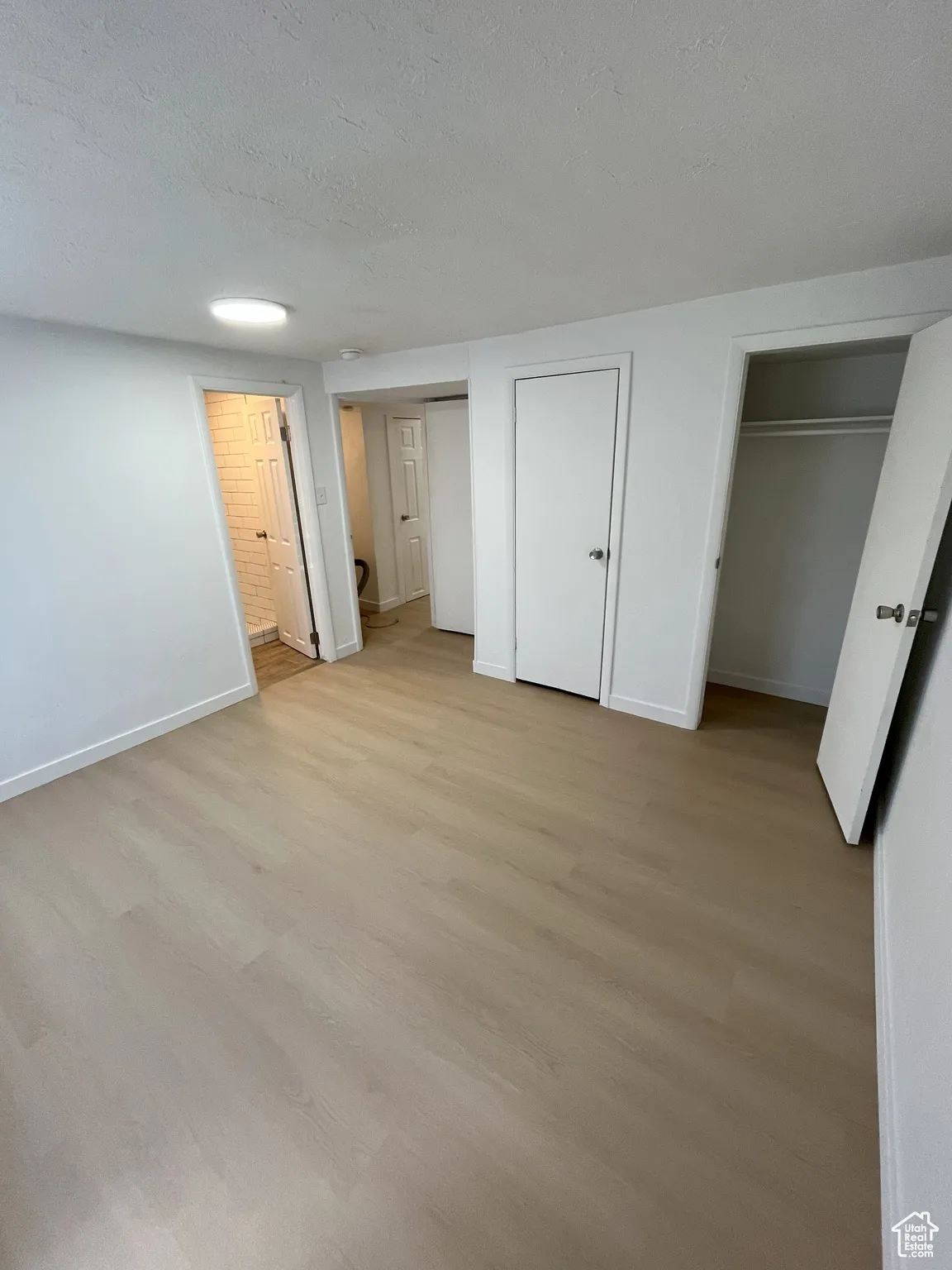 Unfurnished bedroom featuring light wood-type flooring, multiple closets, a textured ceiling, and connected bathroom