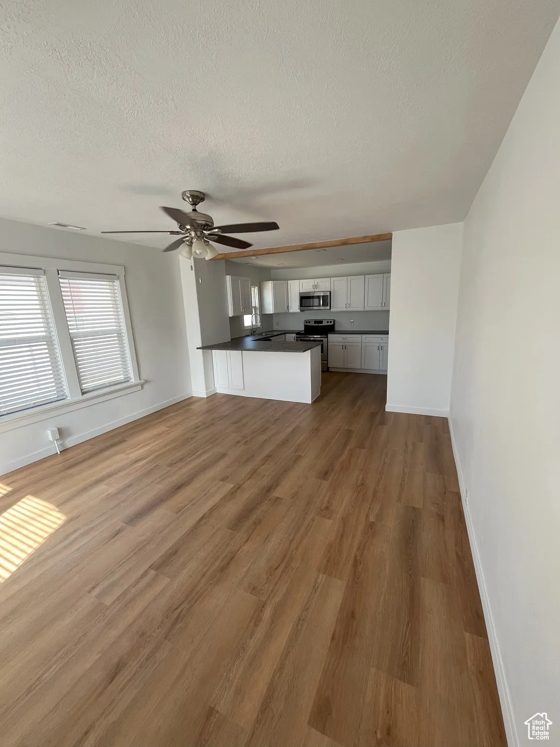 Unfurnished living room featuring dark wood-style flooring, a textured ceiling, and a ceiling fan