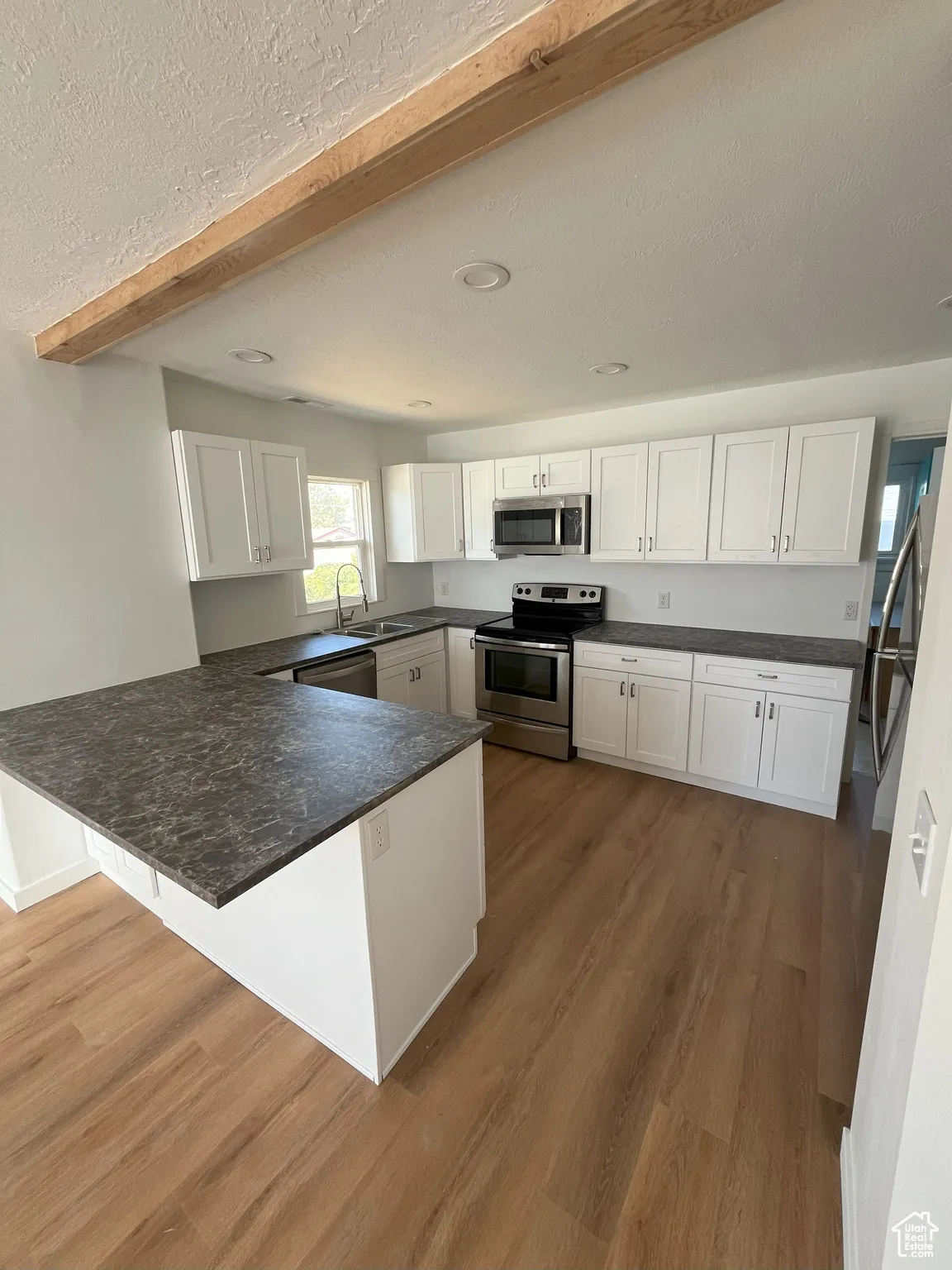 Kitchen featuring appliances with stainless steel finishes, dark wood-type flooring, a peninsula, white cabinetry, and a textured ceiling