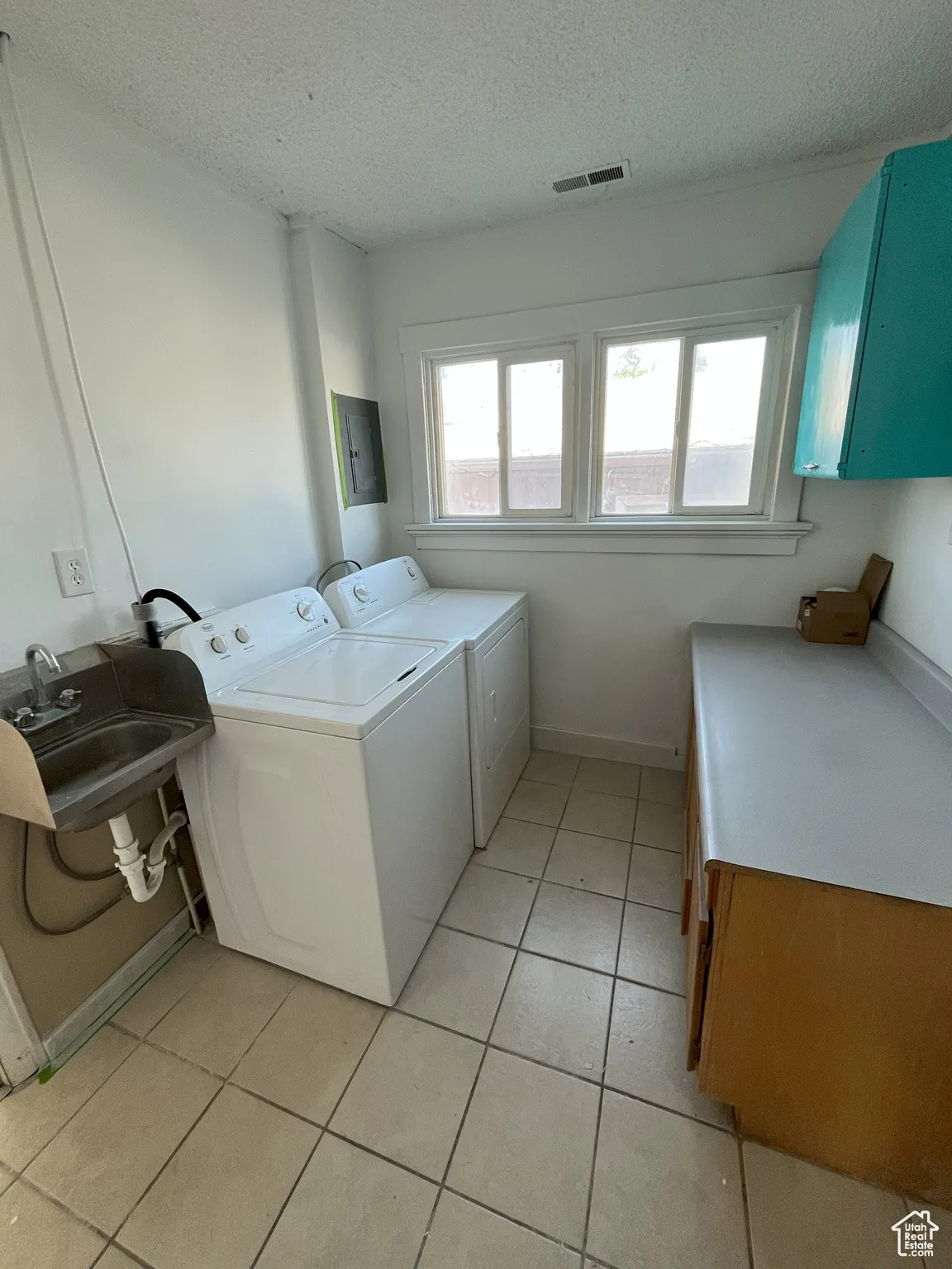 Laundry room with plenty of natural light, a textured ceiling, cabinet space, light tile patterned floors, and washing machine and dryer