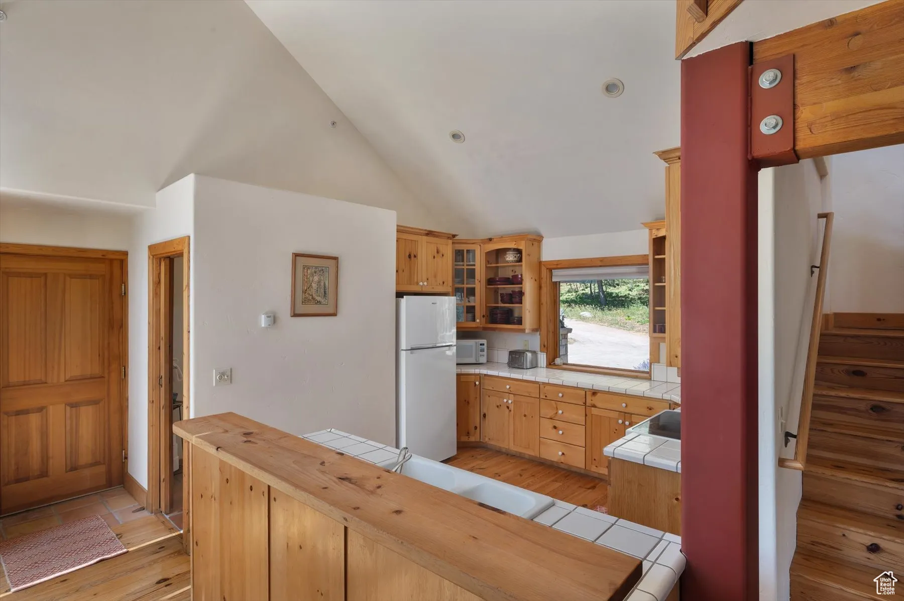 Kitchen with tile counters, white appliances, knotty pine floors, glass insert cabinets, and recessed lighting