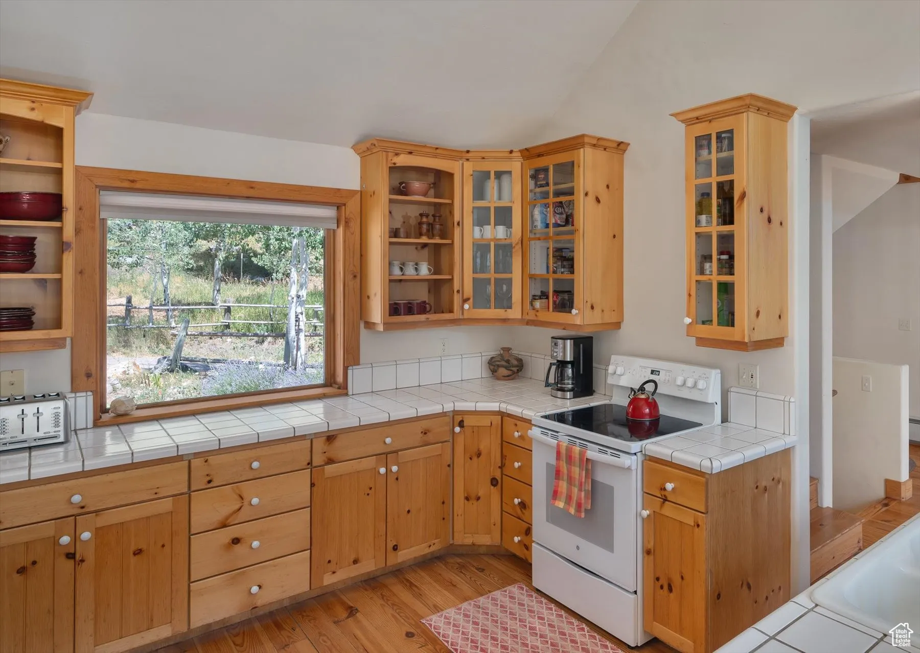 Kitchen with electric stove, open shelves, knotty pine floors, glass insert cabinets, and vaulted ceiling