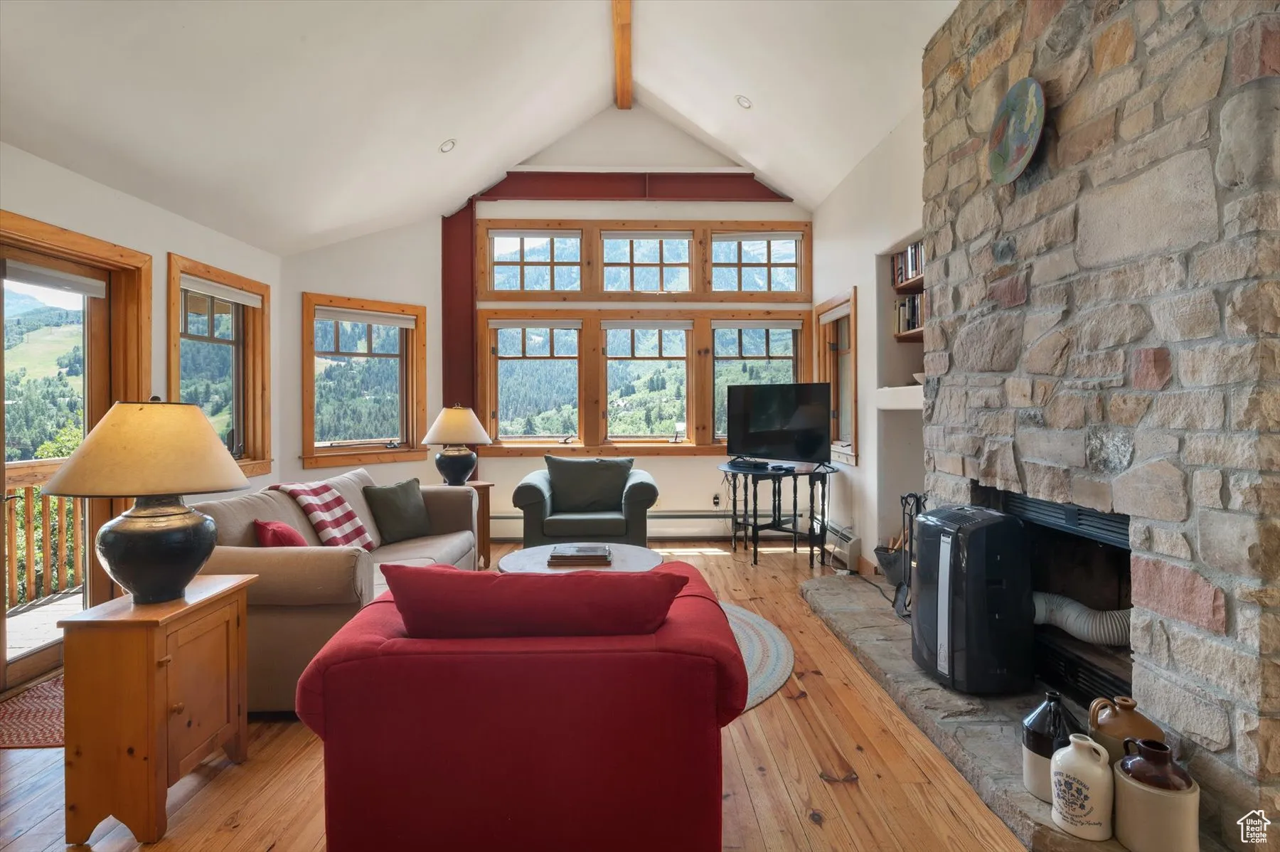 Living room featuring knotty pine floors a stone faced wood burning fireplace, along with walls of windows that lookout to fabulous views. French doors from this room lead out to a covered deck