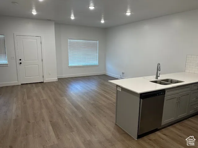 Kitchen featuring gray cabinetry, stainless steel dishwasher, a peninsula, dark wood-type flooring, and light stone counters