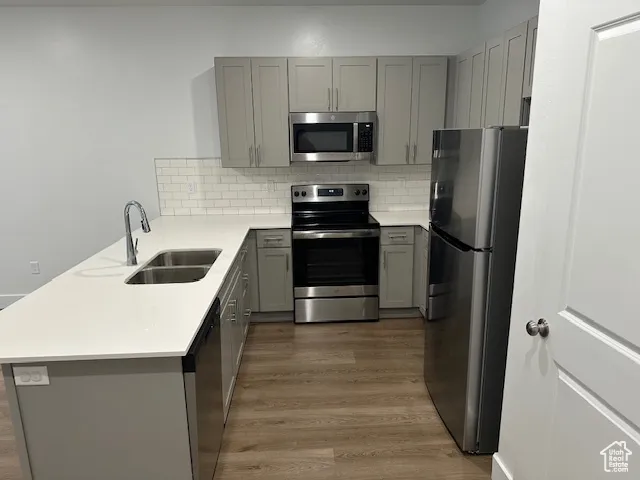 Kitchen with gray cabinets, appliances with stainless steel finishes, tasteful backsplash, light wood finished floors, and a peninsula