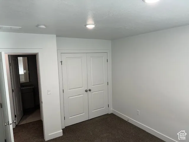 Unfurnished bedroom featuring dark colored carpet, a textured ceiling, and a closet