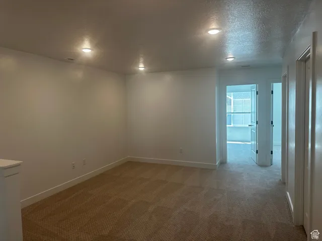 Empty room featuring light colored carpet and a textured ceiling