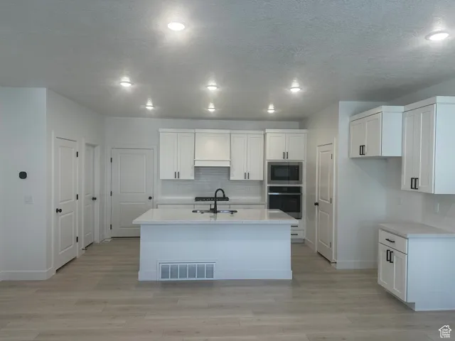 Kitchen with white cabinetry, decorative backsplash, stainless steel appliances, light stone counters, and a textured ceiling