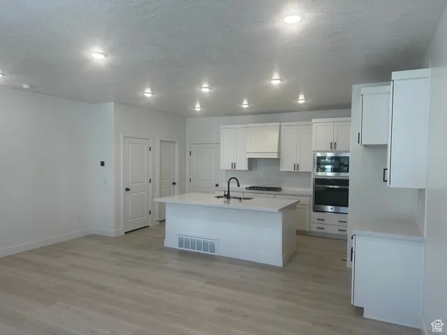 Kitchen featuring stainless steel appliances, decorative backsplash, an island with sink, light stone countertops, and a textured ceiling