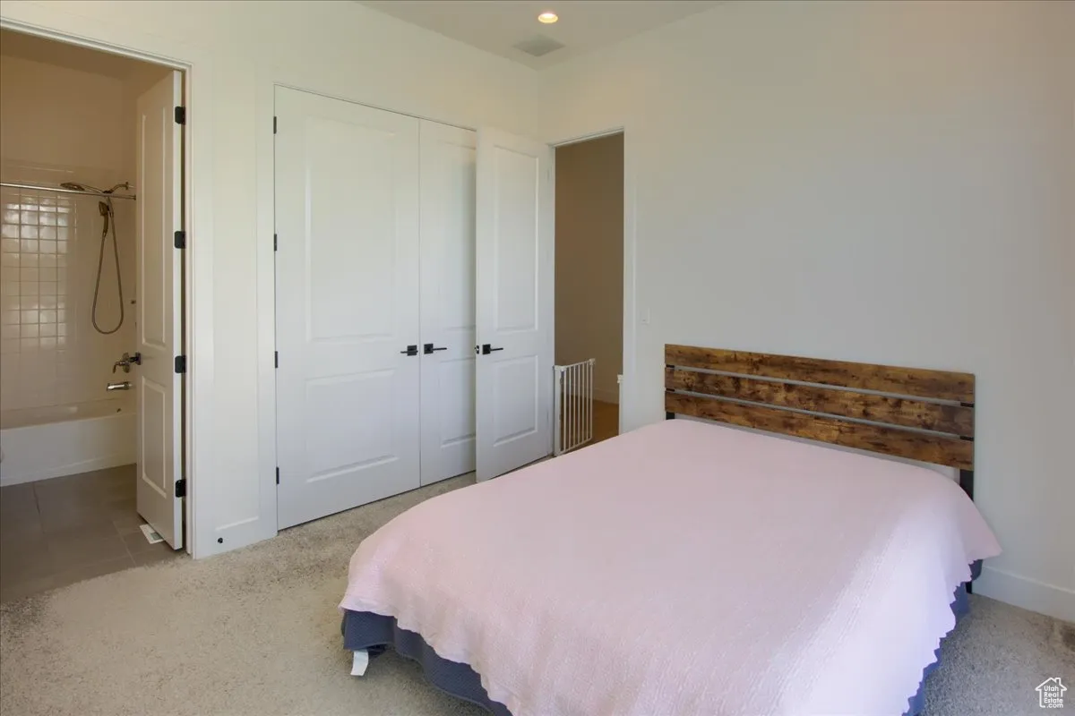 Bedroom with connected bathroom, light colored carpet, a closet, and light tile patterned floors
