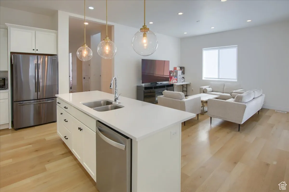 Kitchen with white cabinets, appliances with stainless steel finishes, open floor plan, light wood-style floors, and recessed lighting
