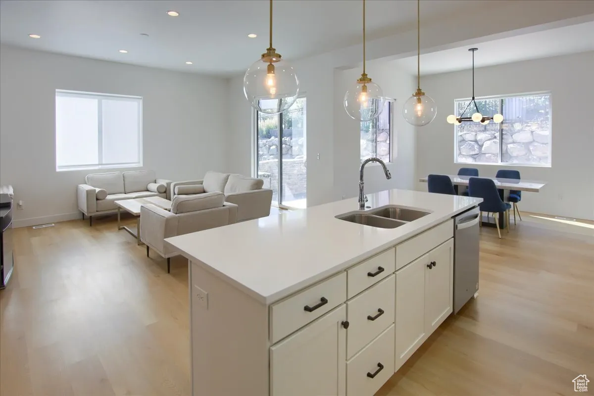 Kitchen with light wood-type flooring, open floor plan, white cabinetry, a kitchen island with sink, and hanging light fixtures