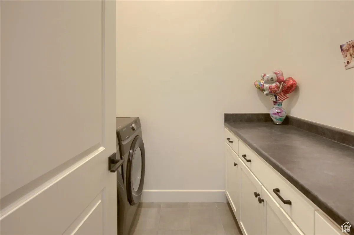 Laundry area with washer / clothes dryer, cabinet space, and light tile patterned flooring