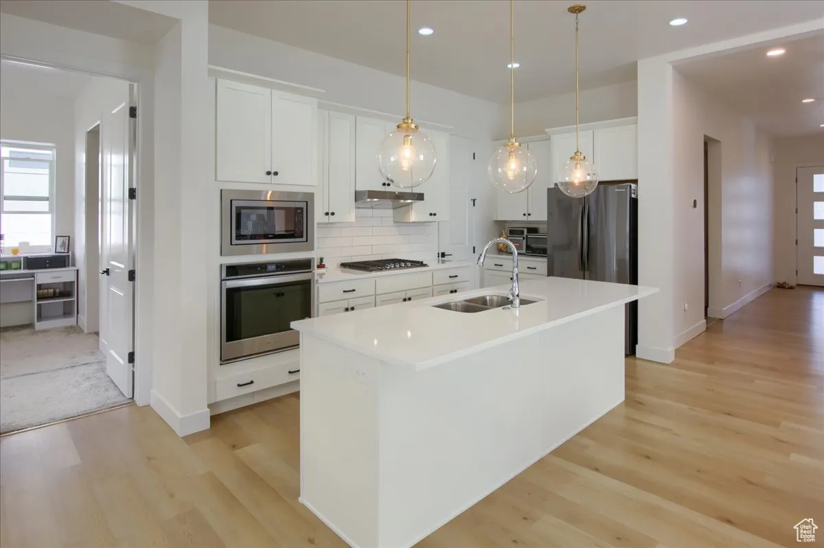Kitchen with a center island with sink, stainless steel appliances, white cabinets, decorative light fixtures, and recessed lighting