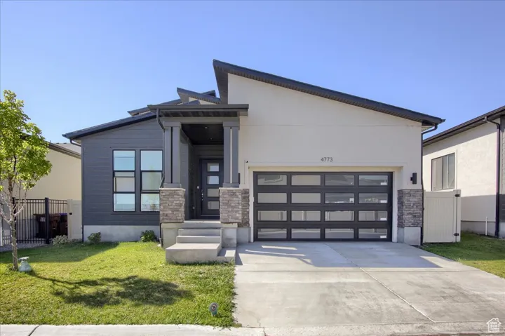 Contemporary home featuring stone siding, a garage, and driveway