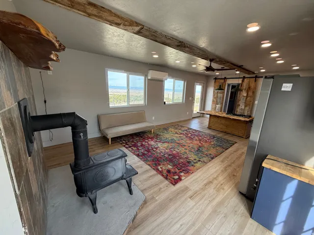 Living area with light wood-type flooring, beamed ceiling, a wood stove, recessed lighting, and a ceiling fan