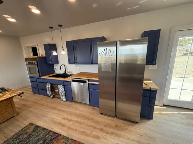 Kitchen featuring blue cabinets, stainless steel appliances, wooden counters, light wood-style flooring, and hanging light fixtures