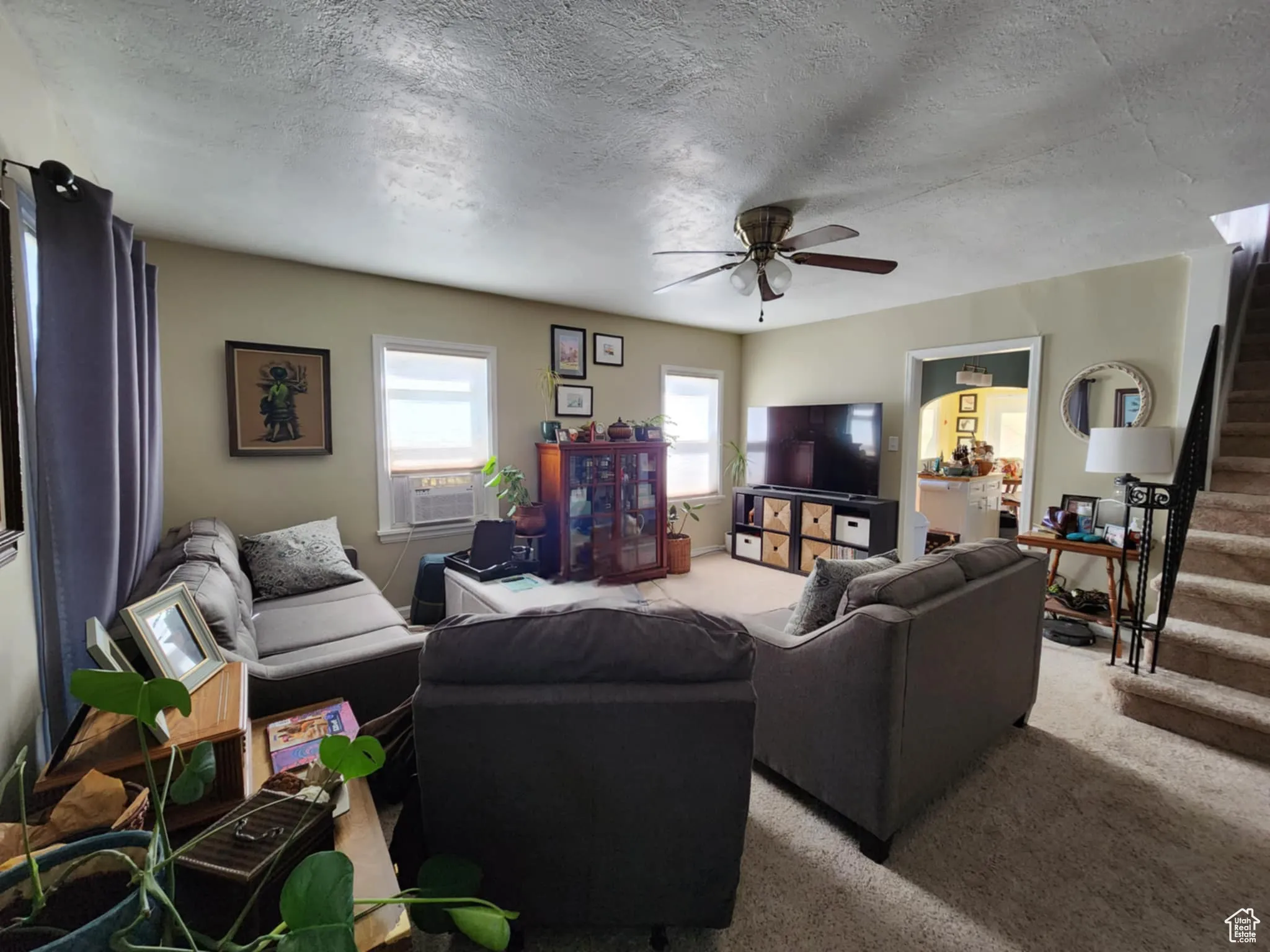 Living room featuring stairs, carpet floors, a textured ceiling, a ceiling fan, and cooling unit