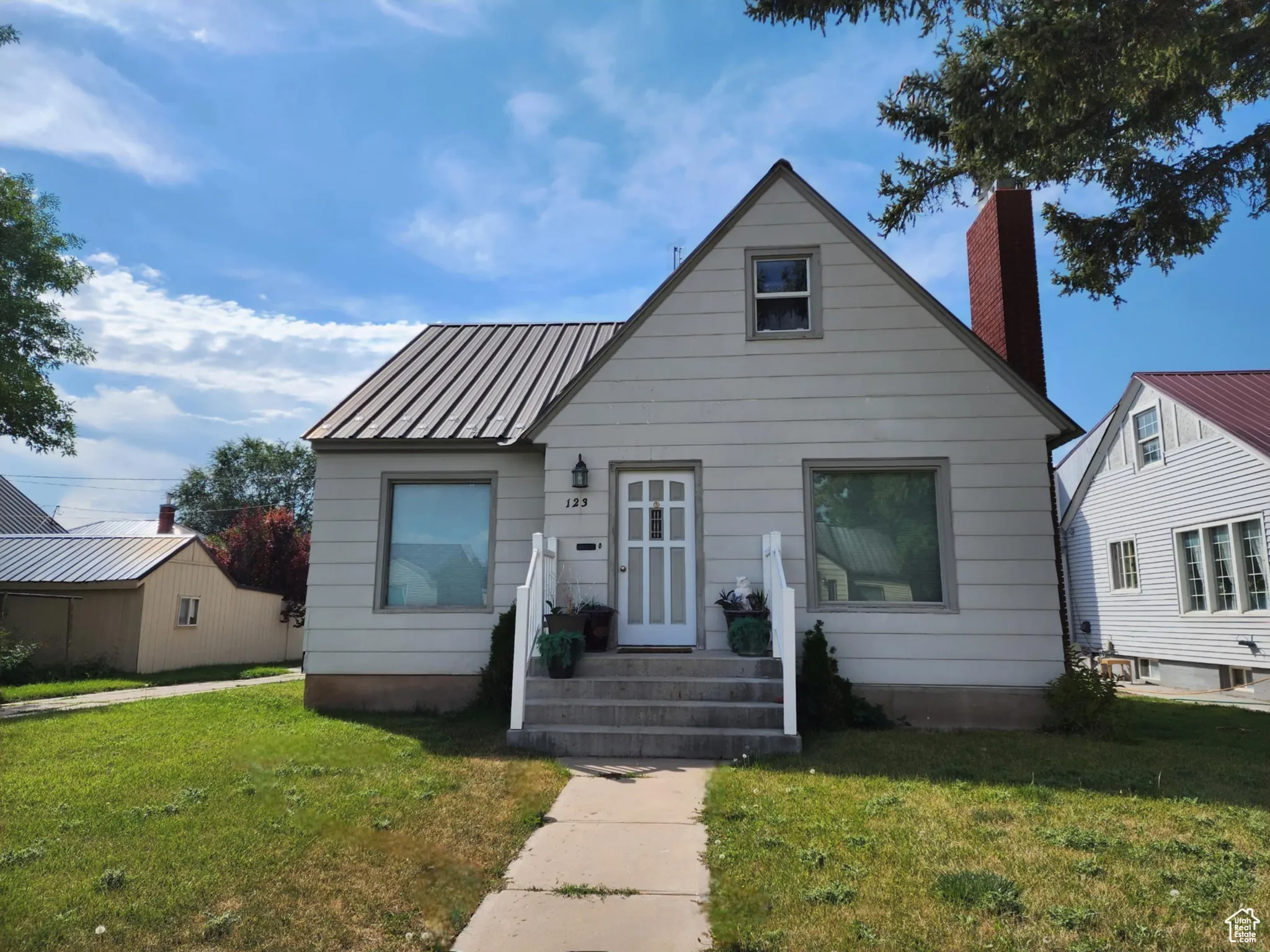 Bungalow-style home featuring a front lawn, a chimney, and a metal roof