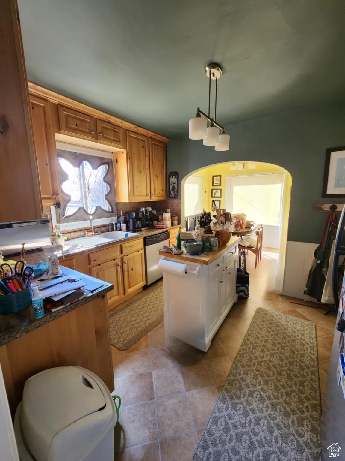 Kitchen with arched walkways, a wainscoted wall, stainless steel dishwasher, hanging light fixtures, and light tile patterned flooring