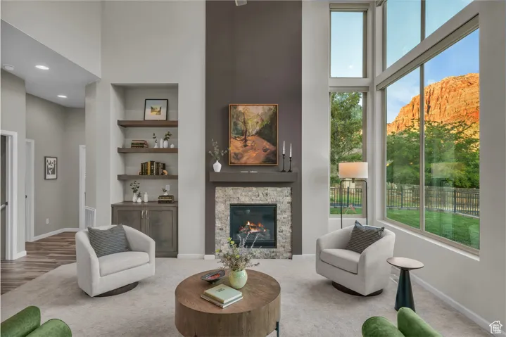 Living room featuring a high ceiling, a fireplace, built in shelves, and carpet flooring