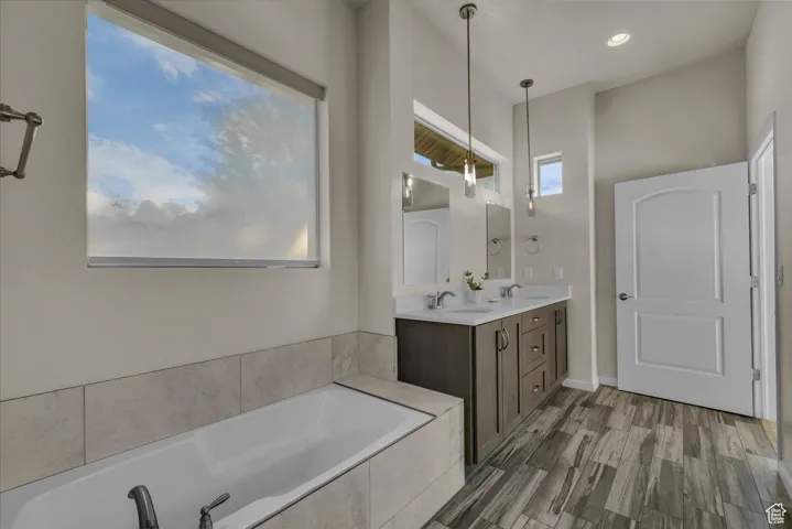 Full bathroom featuring double vanity, a garden tub, and dark wood-style floors