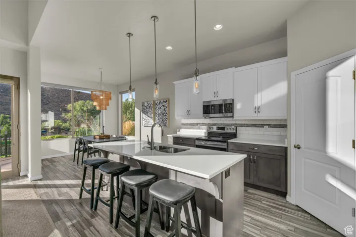 Kitchen with backsplash, white cabinetry, appliances with stainless steel finishes, hanging light fixtures, and a breakfast bar area