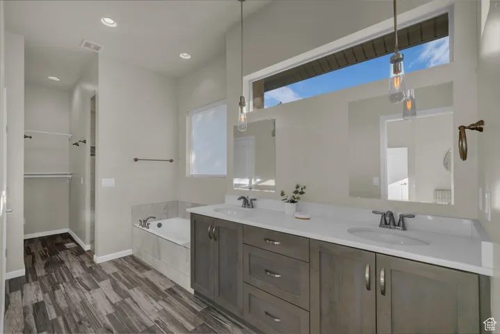 Bathroom featuring a garden tub, double vanity, recessed lighting, dark wood-type flooring, and a closet