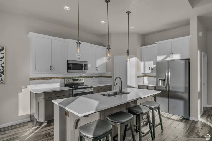 Kitchen featuring decorative backsplash, appliances with stainless steel finishes, pendant lighting, an island with sink, and a breakfast bar area