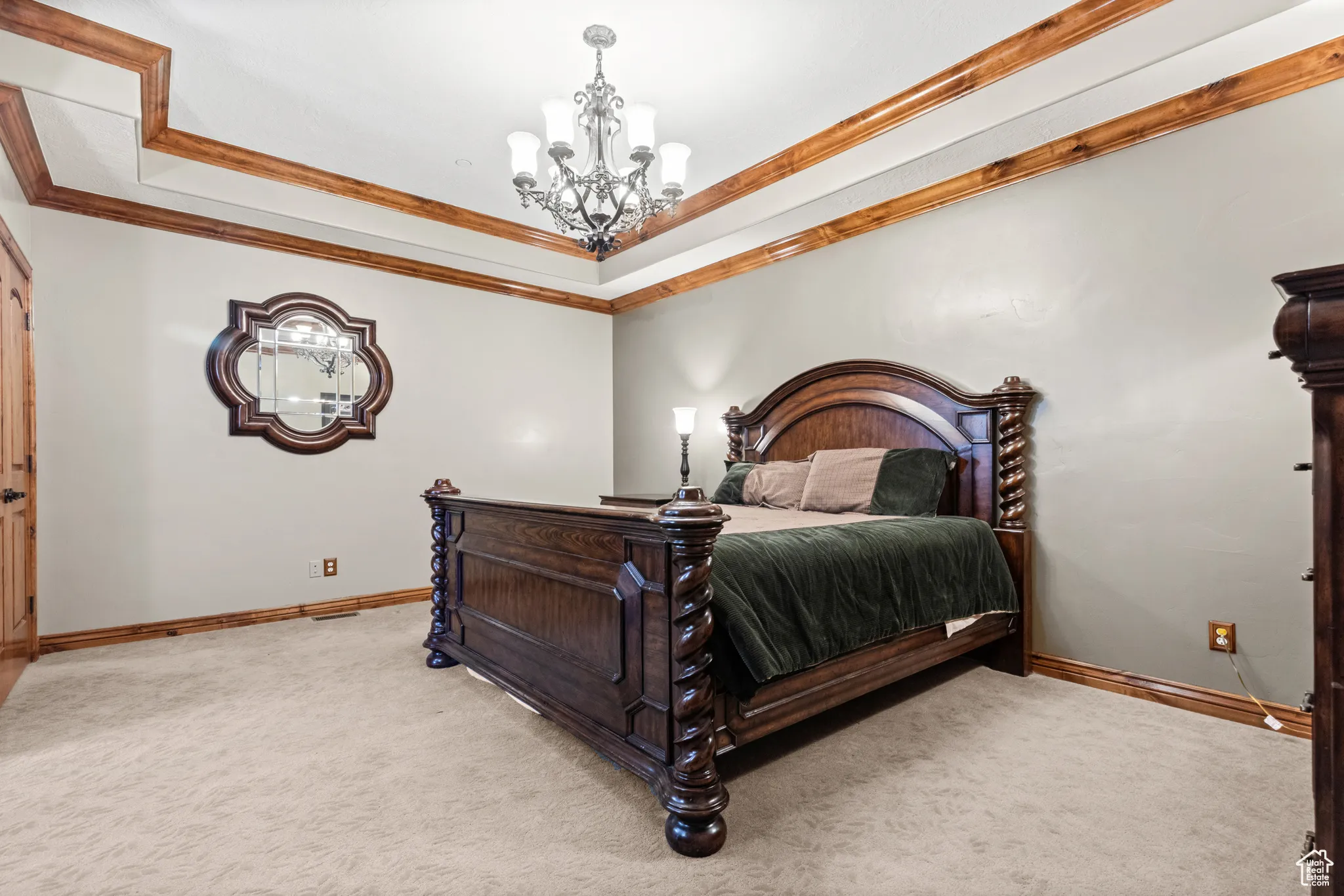 Bedroom with ornamental molding, light carpet, a tray ceiling, and a chandelier