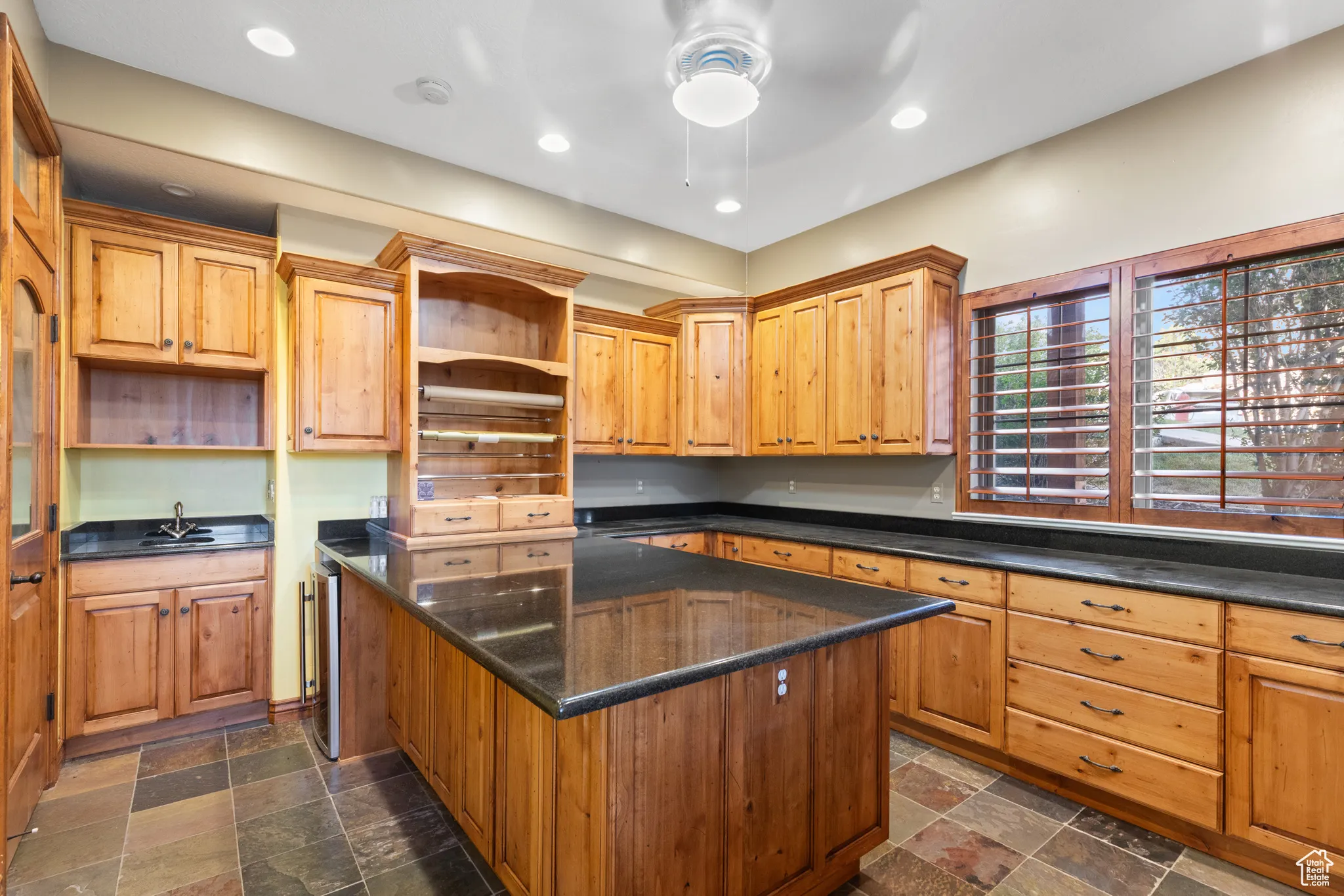 Kitchen featuring open shelves, a center island, recessed lighting, and dark stone finish floors