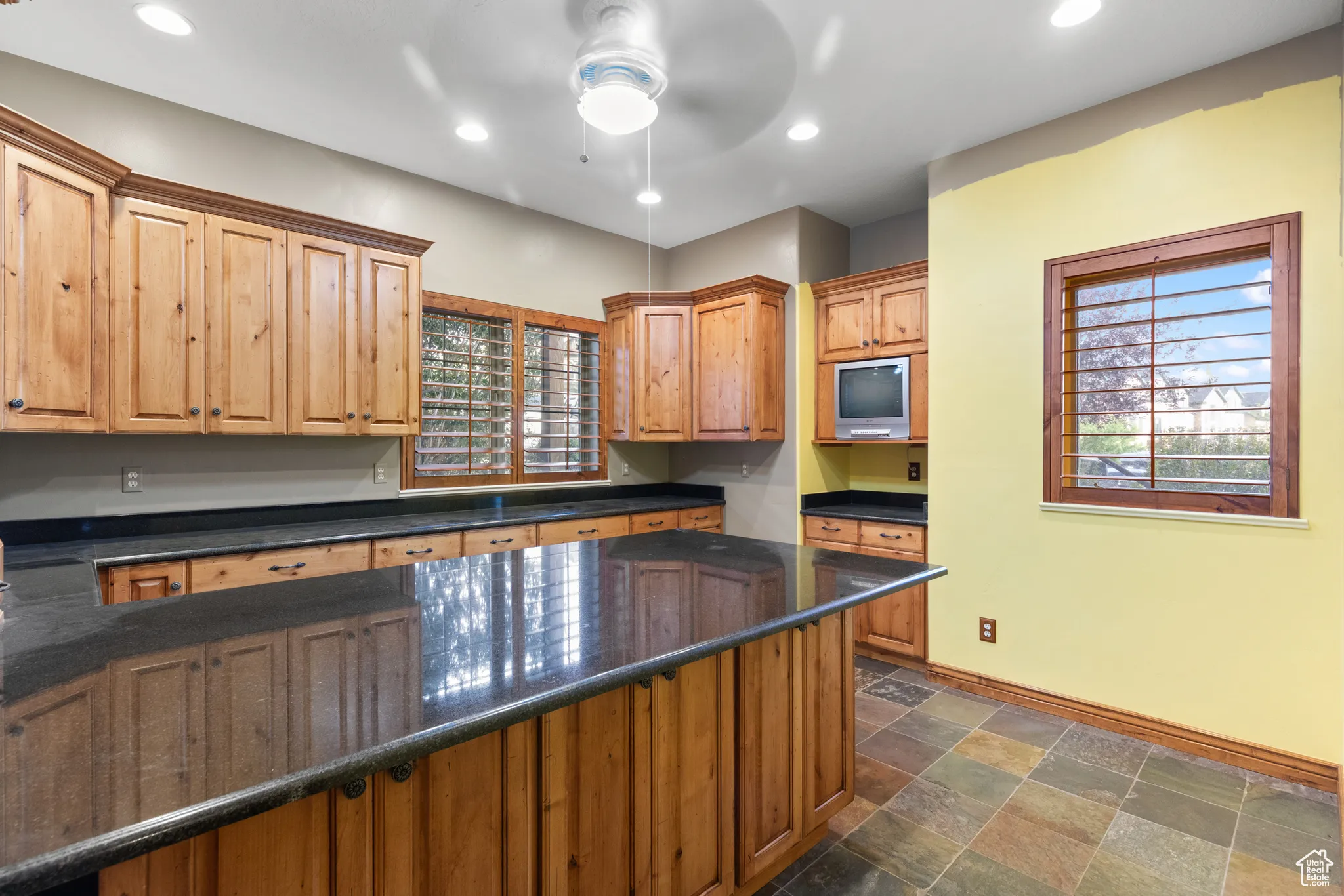 Kitchen with recessed lighting, dark stone finish floors, ceiling fan, dark stone countertops, and brown cabinetry