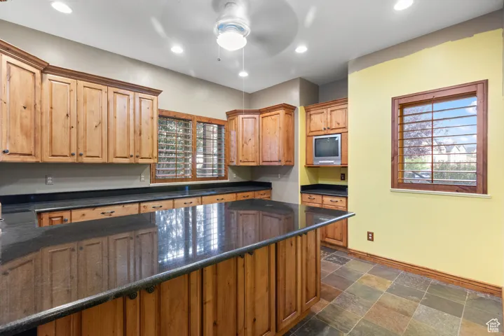 Kitchen with recessed lighting, dark stone finish floors, ceiling fan, dark stone countertops, and brown cabinetry