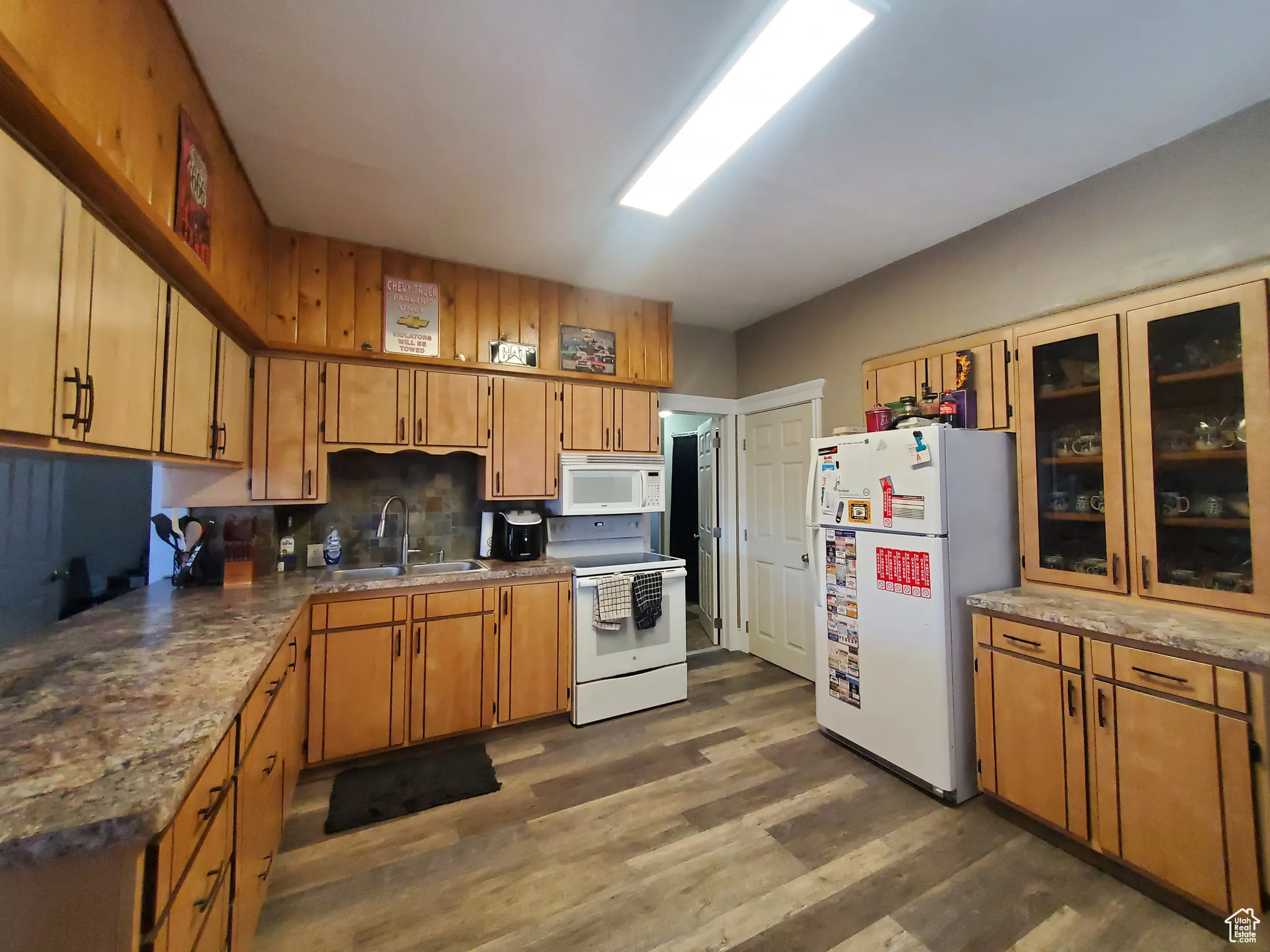 Kitchen with white appliances, dark wood-type flooring, decorative backsplash, glass insert cabinets, and new countertops.