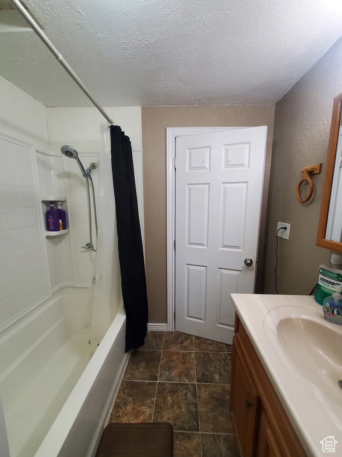 Bathroom with a textured ceiling, vanity, shower / bath combination with curtain, and a textured wall